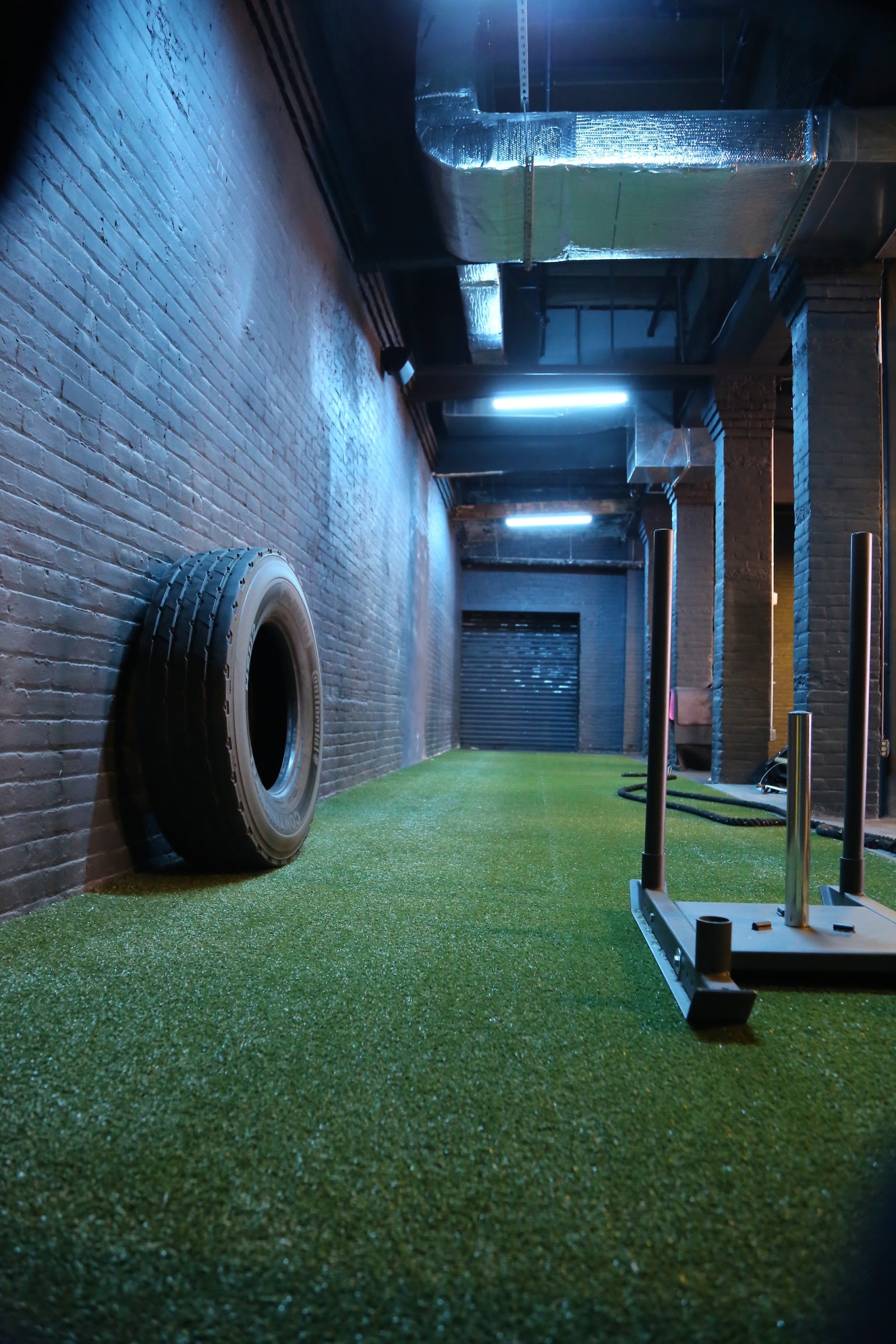 Turf sled lane along a brick wall, with a tire and a sled